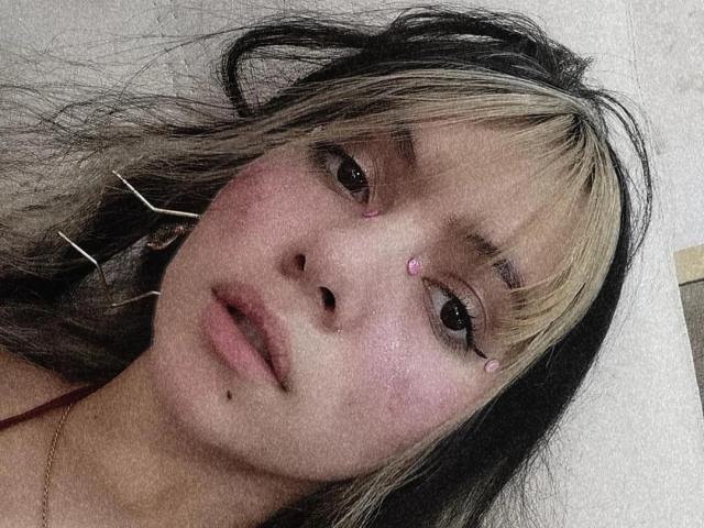 ElizabethBlizz ha capelli biondi e neri con frangia liscia, piccoli puntini rosa sul naso e sulla fronte, e una piccola macchia sulla guancia. Indossa una sottile collana..