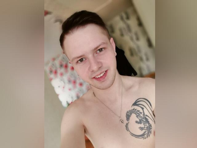 MikeXKing, sin camisa, sonriendo, cabello castaño corto, ojos verdes, pequeño aro en la nariz, collar, tatuaje en el pecho derecho, hombros desnudos, piel pálida, ligero vello facial, interior, parte superior del cuerpo, selfie..