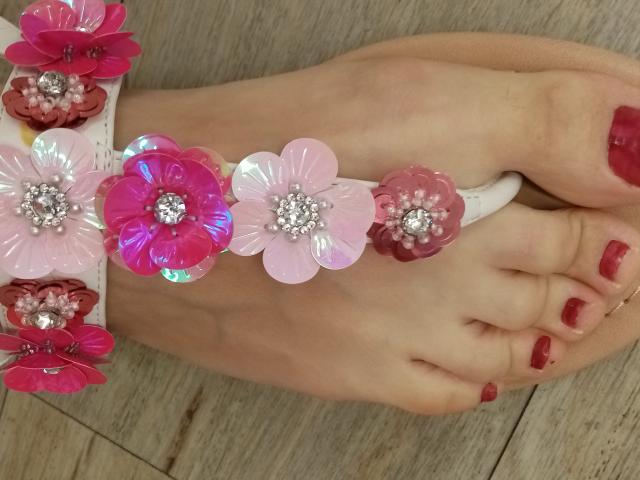 ASexyLady's feet with red-painted toenails, wearing a white ankle bracelet adorned with pink and red plastic flowers with sparkling centers, on a wooden floor.