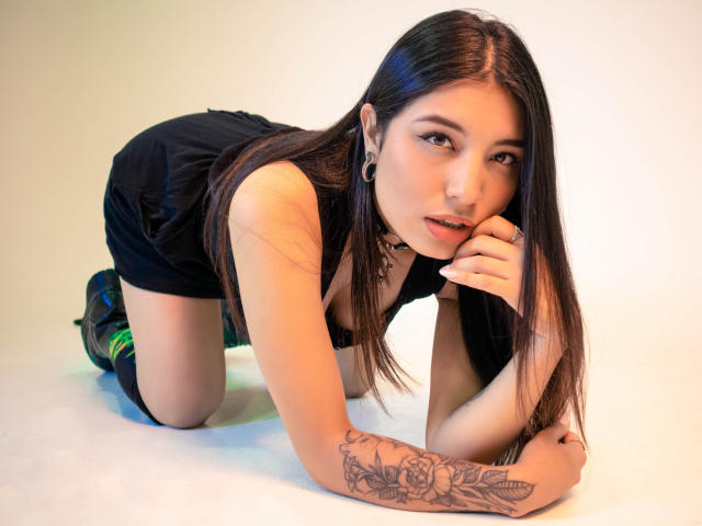 LorenDiaz à quatre pattes, robe noire, collier, chaussettes vertes, bras tatoué, longs cheveux foncés, regardant la caméra, main sur le menton, bottes noires, sexy, attirante, peau claire..