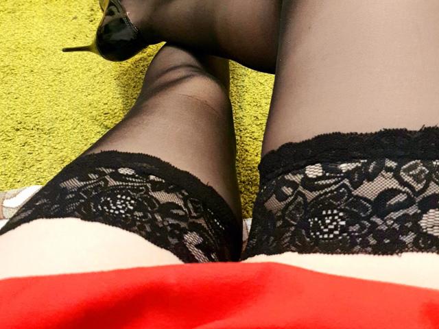 Le calze nere con pizzo di Anna Fock, abbinate ai tacchi alti neri, insieme al suo vestito rosso, mostrano le sue cosce scoperte e il motivo a pizzo nero sulle calze..