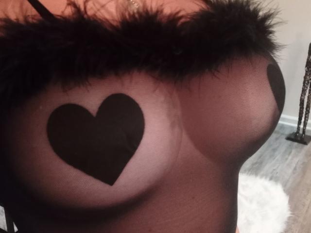 La blusa negra lisa de EvaRodinson, con pequeños cubrebustos negros en forma de corazón sobre sus pechos, presenta un borde negro de pelo. Sus pezones son ligeramente visibles a través de la tela..