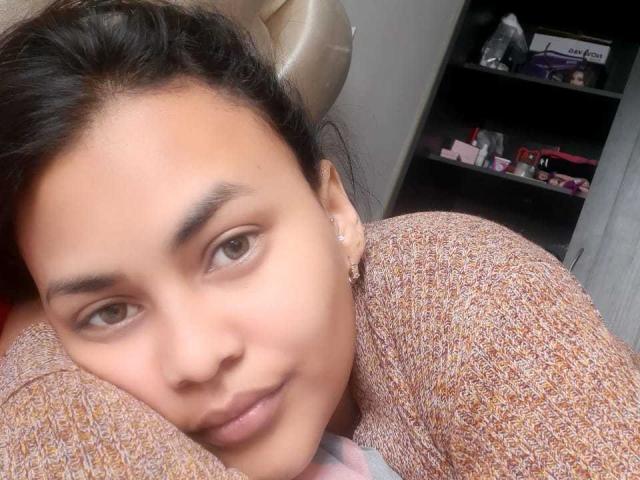 IssaHabib's face with brown eyes, dark eyebrows, and light brown skin. She's wearing a brown, textured sweater, lying down with a slight smile, and a small earring.
