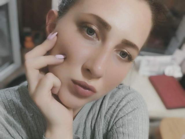 Katerina Pits tiene una expresión seria, piel clara y uñas rosadas, toca su mejilla con una mano, lleva una camiseta gris de punto, tiene ojos marrones y una ligera expresión de ceño fruncido..