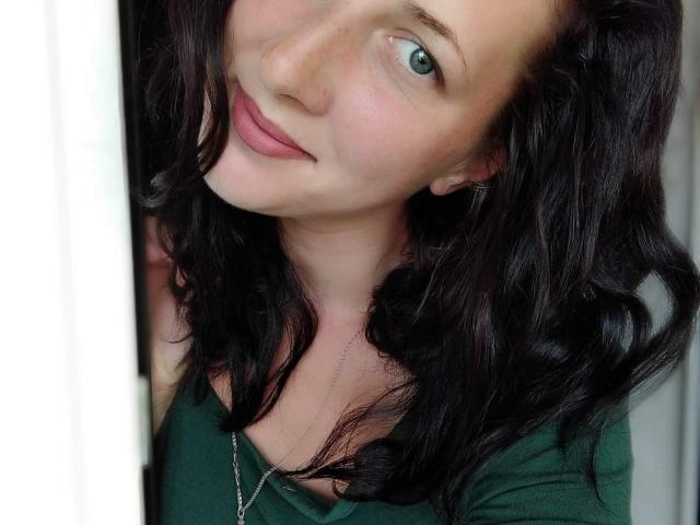 Katerina Pits heeft golvend zwart haar, groene ogen en roze lippen, draagt een groene top met een zilveren ketting en glimlacht zachtjes naar de camera..
