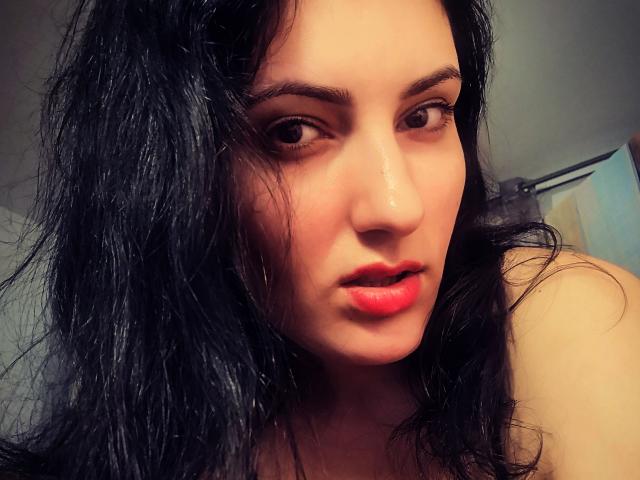 AddictedToUTS has dark, wet-looking hair, brown eyes, and red lipstick. Their skin is light with a slight sheen. They're looking slightly to the side with a neutral expression.