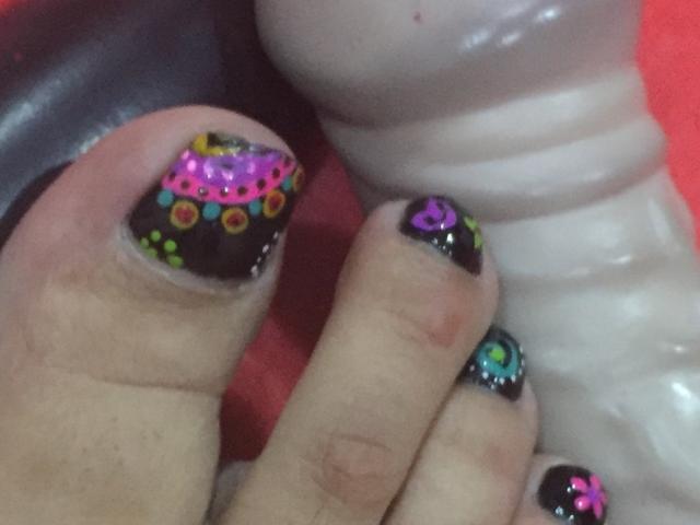 AmbarSimmons's toes with black nail polish, colorful glitter, and pink rhinestones, holding a white dildo, showing off a shiny, textured surface.