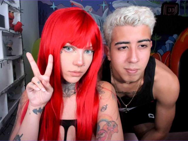 HardCoreSexy with bright red hair, tattoos, and a nose ring, making a peace sign, next to HardCoreSexy with bleached hair, black tank top, and a necklace.