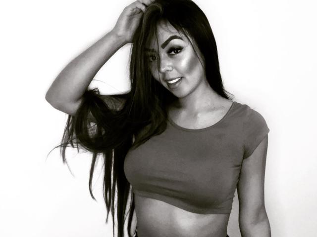 EvaBrown with long dark hair, hand in hair, smiling, wearing a tight crop top, showing her tits, monochrome, attractive, confident, sexy.