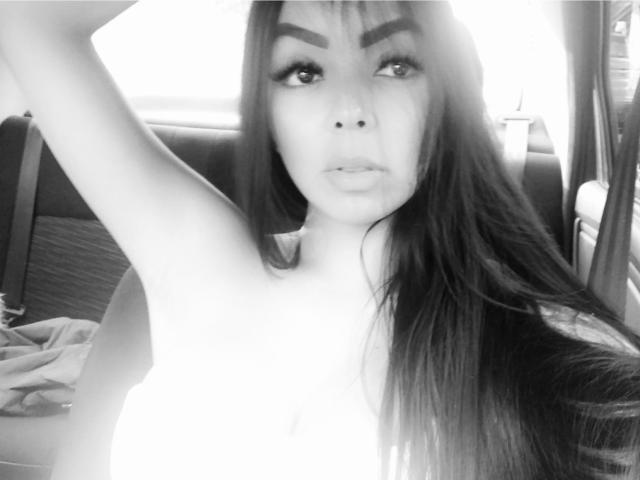 Autoportrait en noir et blanc d'EvaBrown, avec de longs cheveux, un bras levé, des sourcils épais et des lèvres entrouvertes, montrant ses épaules nues et sa partie supérieure de la poitrine, avec un eye-liner et du mascara visibles..