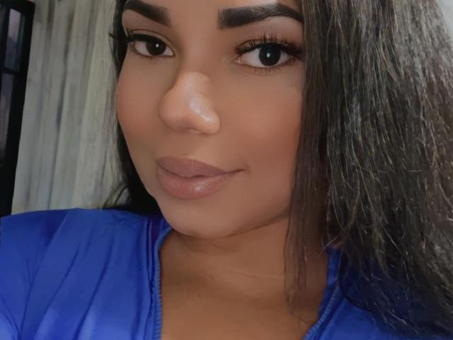 AbellaPhill's face, brown skin, long dark hair, thick eyebrows, full lips, blue top, slight smile, black eyes, looking at camera, cute, sexy, attractive, perfect makeup, soft lighting.
