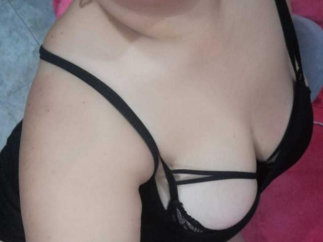 AmbarSimmons has fair skin and black lingerie with strappy detail, showing her tits and cleavage. Her shoulder and part of her chest are visible.