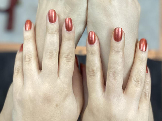 ArleenHunter's hands with shiny red metallic nail polish, fingers spread, showing off her well-manicured nails against a blurred background. Her skin is pale and smooth.