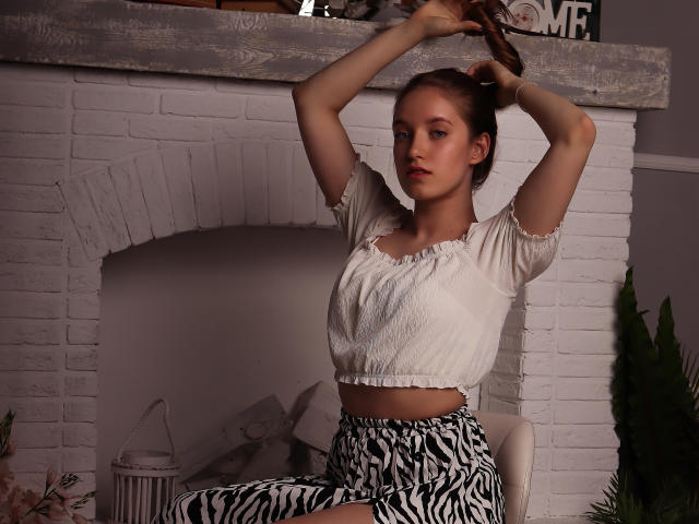 EvaPink, con piccoli seni, top corto a maniche gonfie bianche, pantaloni a motivi zebrati, braccia alzate, treccia marrone, espressione neutra, seduta, camino in mattoni bianchi, illuminazione interna soffusa..