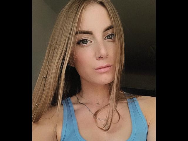 BlondyOneSex tiene el pelo rubio largo y liso, ojos verdes, una nariz pequeña y labios rosados. Lleva una camiseta azul sin mangas y un collar de plata. Sus pechos son visibles..