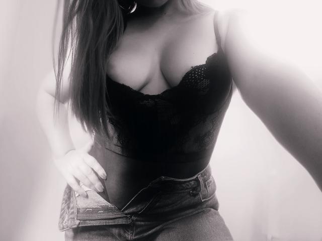 KimFire con i capelli lunghi, indossa un corpetto di pizzo nero, mostrando il seno, mentre scucce la cerniera dei jeans, con una mano sulla vita, in un selfie in bianco e nero..