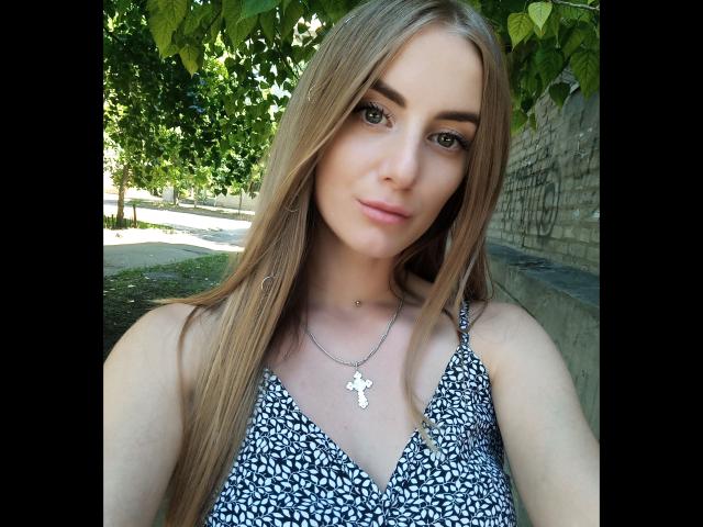 BlondyOneSex ha lunghi capelli biondi, occhi verdi e indossa un abito a pois neri e bianchi con una collana d'argento a forma di croce. Il seno è visibile sotto l'abito..