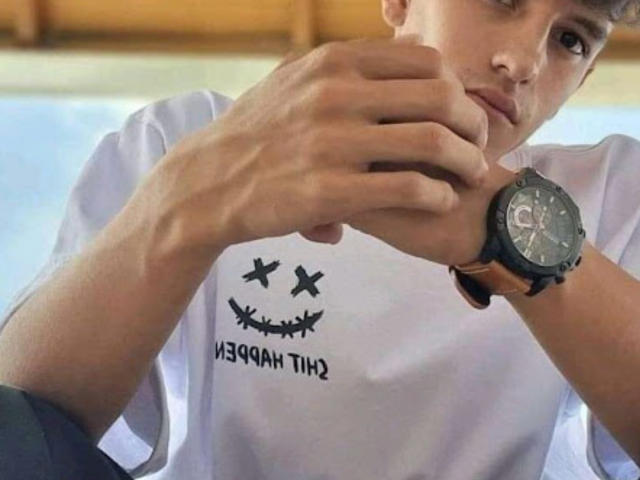 SuperXTenty tenant une montre noire avec un cadran rond, portant une chemise blanche avec un motif graphique noir, regardant légèrement sur le côté, avec une expression calme..