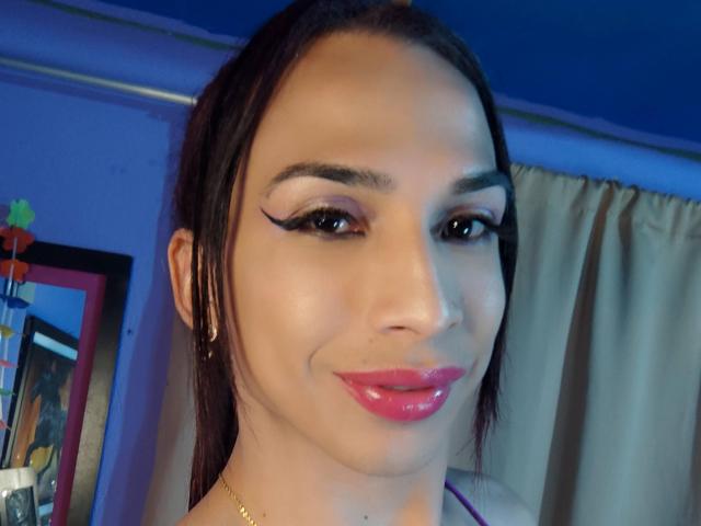 Ein Selfie von brunettehot77 mit glänzenden, rosafarbenen Lippen, Eyeliner im "Winged"-Stil und einem leichten Lächeln, das ihr geschminktes Gesicht und ihre braunen Haare im Pferdeschwanz zeigt..