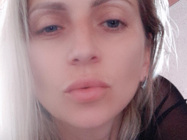 AliaAnita hat eine helle Haut, blaue Augen und volle, rosafarbene Lippen. Ihr blondes Haar bedeckt teilweise ihr Gesicht. Sie trägt ein schwarzes Hemd. Ihre Nase ist klein und niedlich..