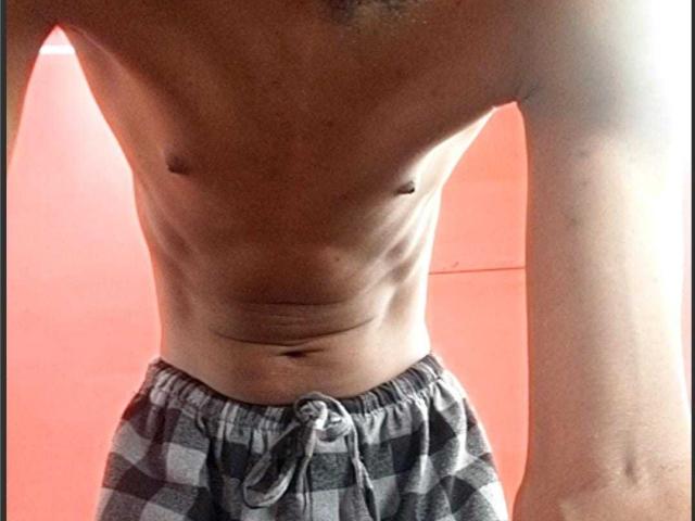 O torso nu, tonificado e de pele morena de LongDickService69, com abdominais visíveis, pequenos mamilos e um leve umbigo. Vestindo calças quadriculadas cinzas e pretas com cintura larga..