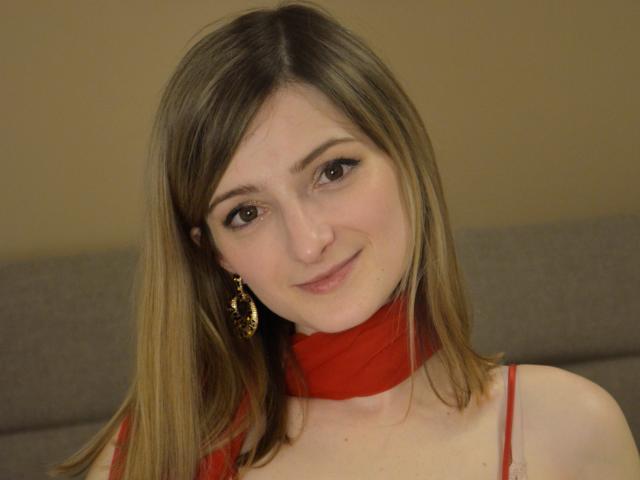 AriaMermaid with blonde hair, red scarf, and gold earrings, smiling at the camera, showing her tits slightly, in a casual, cute, and sexy manner.
