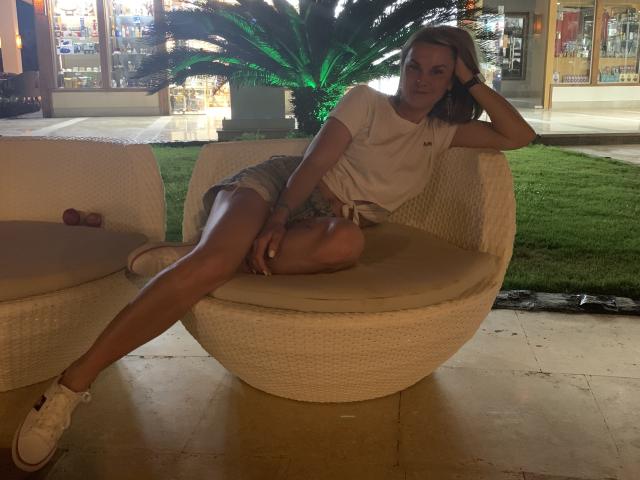 BelleLisaG with blonde hair, white t-shirt, and denim shorts, lounging in a wicker chair, legs spread, showing her ass, white sneakers, relaxed, right hand on head.