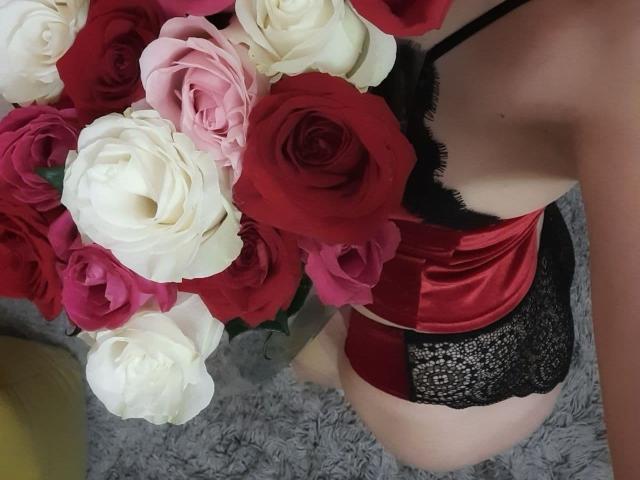 AnnieXCute's red satin and black lace panties, showing her ass, with a bouquet of red, pink, and white roses in the foreground.