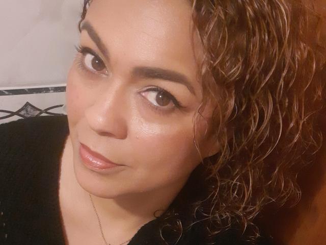 SolmaryHot with wavy brown hair, subtle makeup, glossy lips, and brown eyes, wearing a black top, looking at the camera with a slight smile.