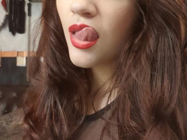 ArleenHunter's face with red lipstick, tongue out, brown wavy hair, light skin, wearing a sheer black top, showing a hint of her tits.