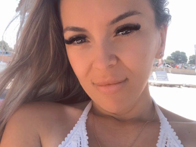 SophieDeee has full, dark eyebrows, long eyelashes, and is looking at the camera with her mouth slightly open. She has light skin, brown hair in a ponytail, and is topless.