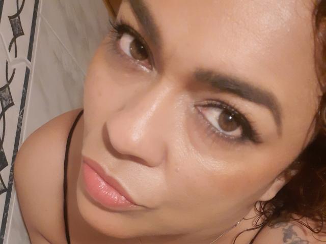 SolmaryHot's face, showing brown eyes, full pink lips, and light brown skin, with curly red hair and a black necklace, looking up with a slightly pouty expression.