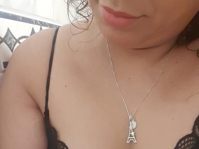 SolmaryHot's upper body, wearing a black lace bra, with a silver necklace featuring a small Eiffel Tower pendant, slightly visible breasts, and a subtle smile.