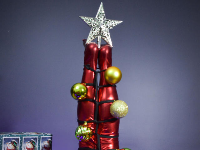 Un sapin de Noël rouge et brillant, avec une étoile scintillante au sommet, décoré de boules dorées et vertes. Une boîte bleue avec des motifs hivernaux se trouve à gauche..