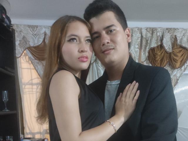 Jake y Megan, con sus senos pegados a un hombre con un traje negro, su mano en su pecho, ambos sonriendo, cabello castaño, labios rosados, su cabello negro corto, camisa gris..
