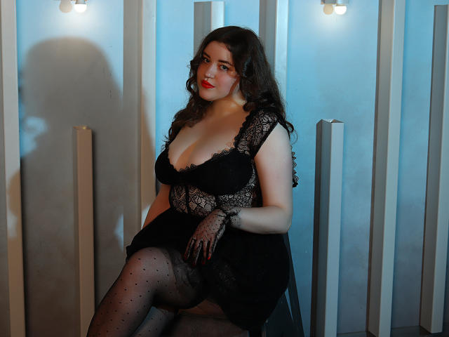 PolinaGrace with big boobs, curvy ass, wearing black lace dress, polka dot tights, and lace gloves, sitting in dim light, looking sexy, with wavy brown hair, red lipstick.
