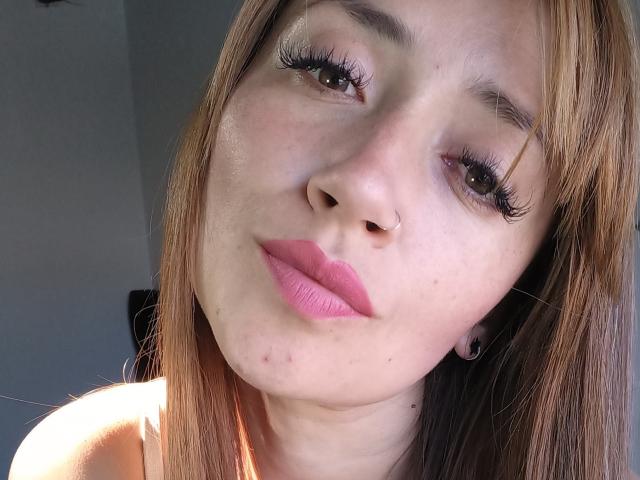 TateSexy a les cheveux brun clair, du rouge à lèvres rose et de longs cils noirs. Elle a une moue, un petit piercing au nez et une légère imperfection sur le visage. Sa peau est légèrement brillante..