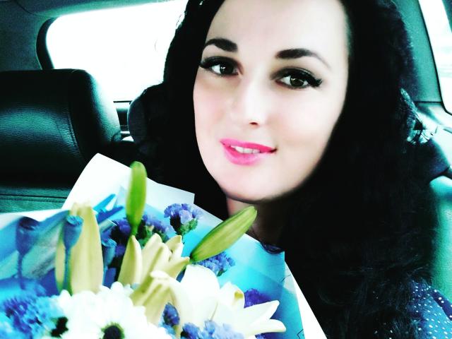 Eine wunderschöne Frau mit dunklen, lockigen Haaren, rosa Lippenstift und schwarzem Eyeliner, die einen Strauß aus weißen, blauen und lila Blumen hält und in einem Auto sitzt..