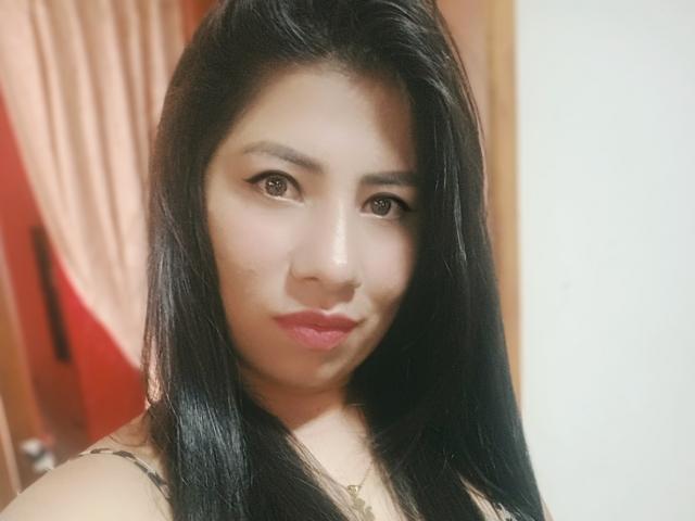 Genesis Thonson, con cabello negro lacio, ojos marrones y lápiz labial rosa, mirando a la cámara con un ligero puchero. Tiene un rostro lindo y lleva puesto un collar..