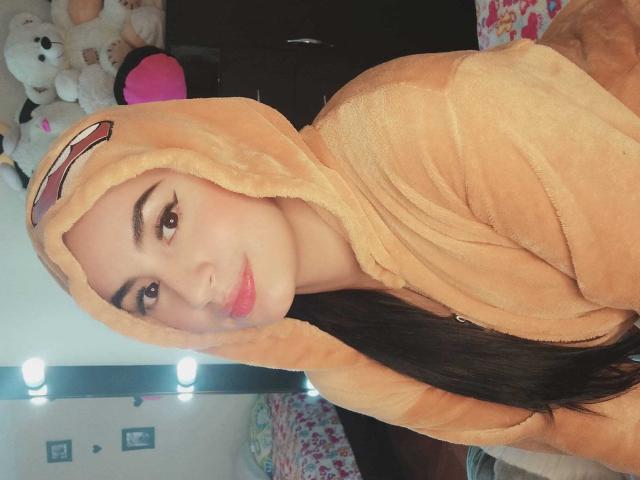MartinaMendezz, avec ses longs cheveux noirs, porte un sweat à capuche Pikachu beige et duveteux. Elle a un visage mignon avec des lèvres roses et regarde l'appareil photo avec un léger sourire..