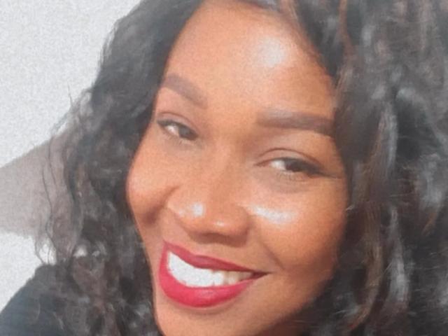 SmithLorie hat dunkles, lockiges Haar, braune Augen, roten Lippenstift und ein glänzendes Gesicht und lächelt mit weißen Zähnen. Ihr Hintern ist nicht sichtbar. Sie trägt schwarze Kleidung..