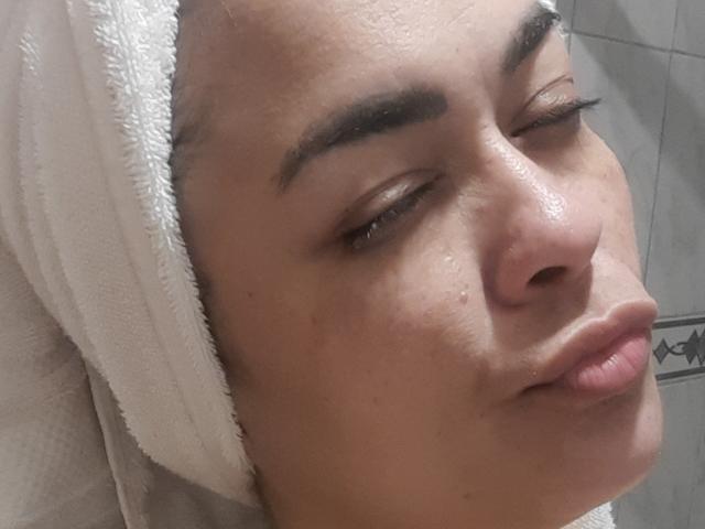 Le visage de SolmaryHot, avec une serviette blanche enroulée autour de la tête, les yeux fermés, un nez légèrement retroussé et un sourire subtil. Elle a des sourcils foncés et une peau légèrement brillante..