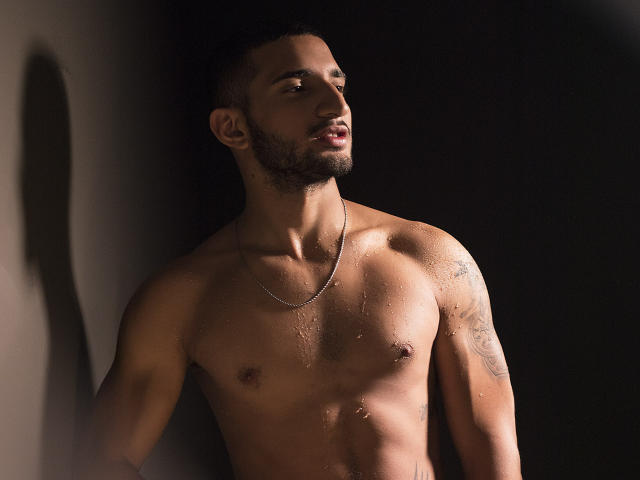 SusiAndMat, sin camisa, de piel oscura, musculosos, tatuajes en el brazo derecho, barba corta, collar de plata, gotas de agua en el pecho, mirando hacia un lado, fondo oscuro, sombra en la pared..