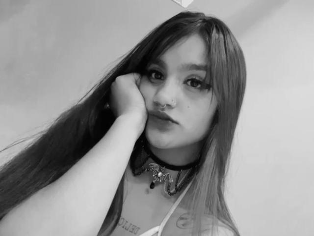Selfie in bianco e nero di GabyDurand con capelli lunghi e lisci, piercing al naso e collana con un design elaborato, con la testa appoggiata sulla mano, che mostra un tatuaggio sul collo. GabyDurand ha un'espressione neutra..