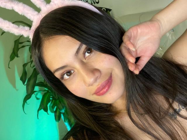AlexaCoeur with long black hair, pink fluffy bunny ears, and pink lips, smiling softly at the camera, touching her ear with one hand.