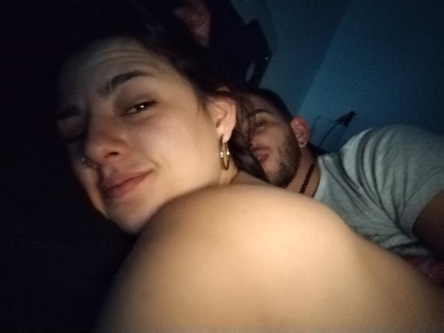Jazmin und Ryan mit entblößtem Gesäß im Vordergrund, helle Haut, kleiner Nasenring und goldene Ohrringe, blicken zu einem bärtigen Mann in einem grauen Hemd zurück, blauer Hintergrund, schwaches Licht..