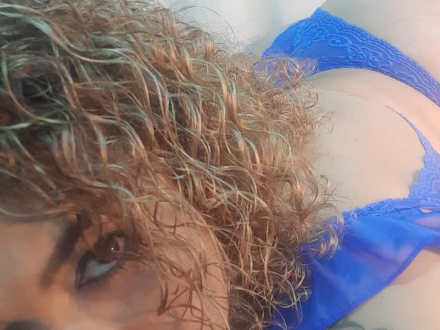 SolmaryHot with curly brown hair, blue lace panties, and visible tits, lying down, focusing on her face and chest. Her eyes are partially visible.