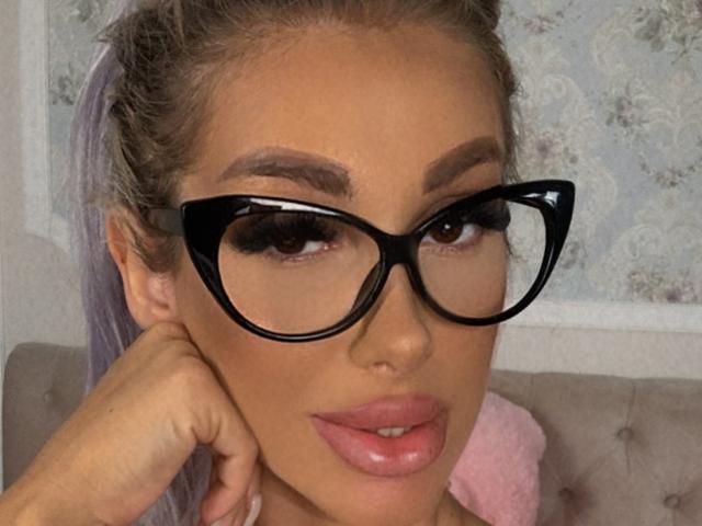 TanyaMonroe with big black-ass glasses, glossy pink lips, and a hand on her face, showing off her sexy brown eyes and well-groomed eyebrows.