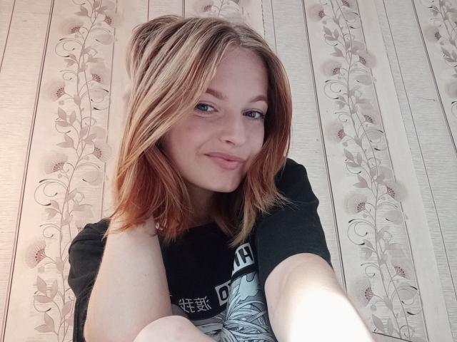Markizza a les cheveux blonds de longueur moyenne, une peau claire et un sourire charmant. Elle porte une chemise noire, et ses petites seins sont légèrement visibles. Elle prend un selfie..