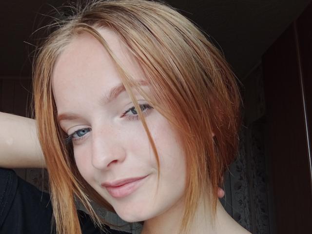 Markizza a les cheveux roux clairs, des yeux bleus et un léger sourire. Elle regarde l'appareil photo avec une expression détendue et confiante. Son bras est levé derrière sa tête..